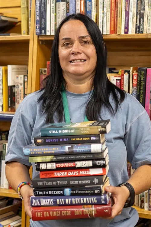 Team member holding a stack of used books in the book department at Value Village Thrift Store.