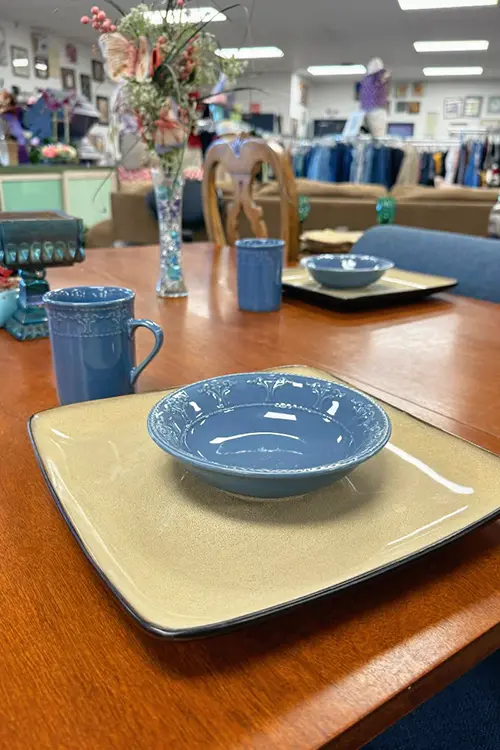 Dinnerware and kitchenware displayed on a dining table inside Value Village Thrift Store.